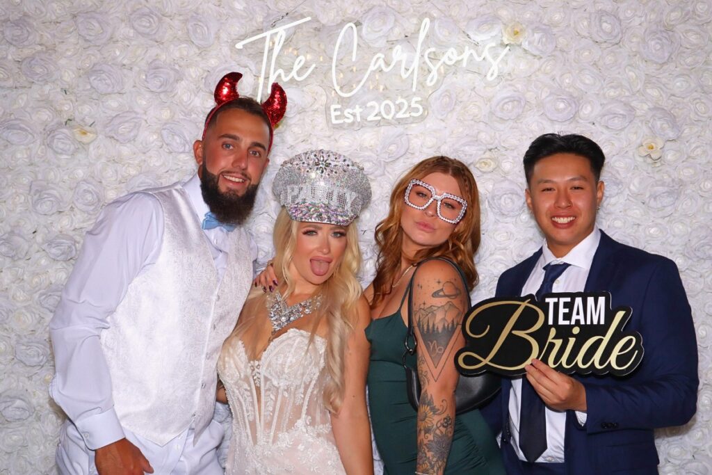 A luxury white rose wall photo booth installation featuring high end floral details for an elevated wedding aesthetic