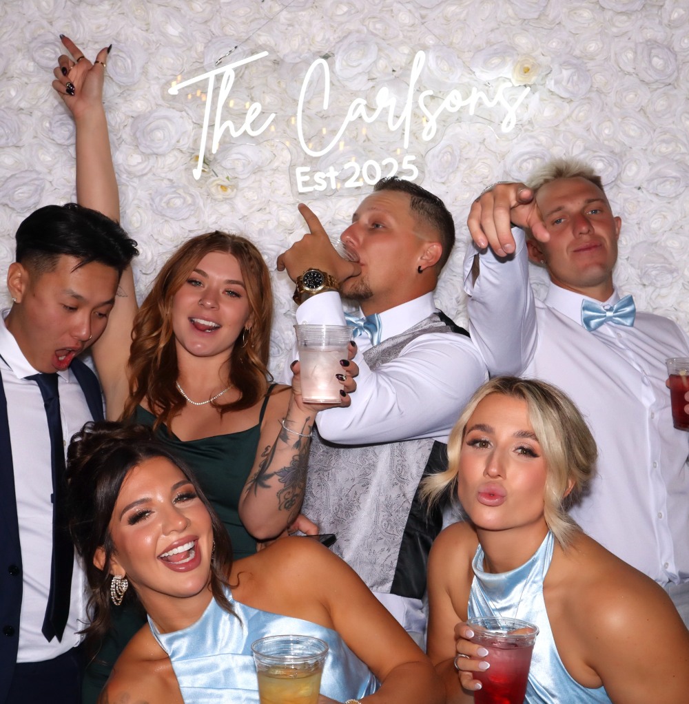 Bridesmaids and groomsmen psoe for a wedding photo booth rental infront of a luxury white rose backdrop at Sanctuary Golf Course in Sedalia Colorado.