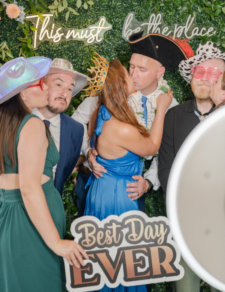 Wedding guests pose in front of a greenery wall backdrop in a party photo booth rental at a wedding in Denver Colorado.